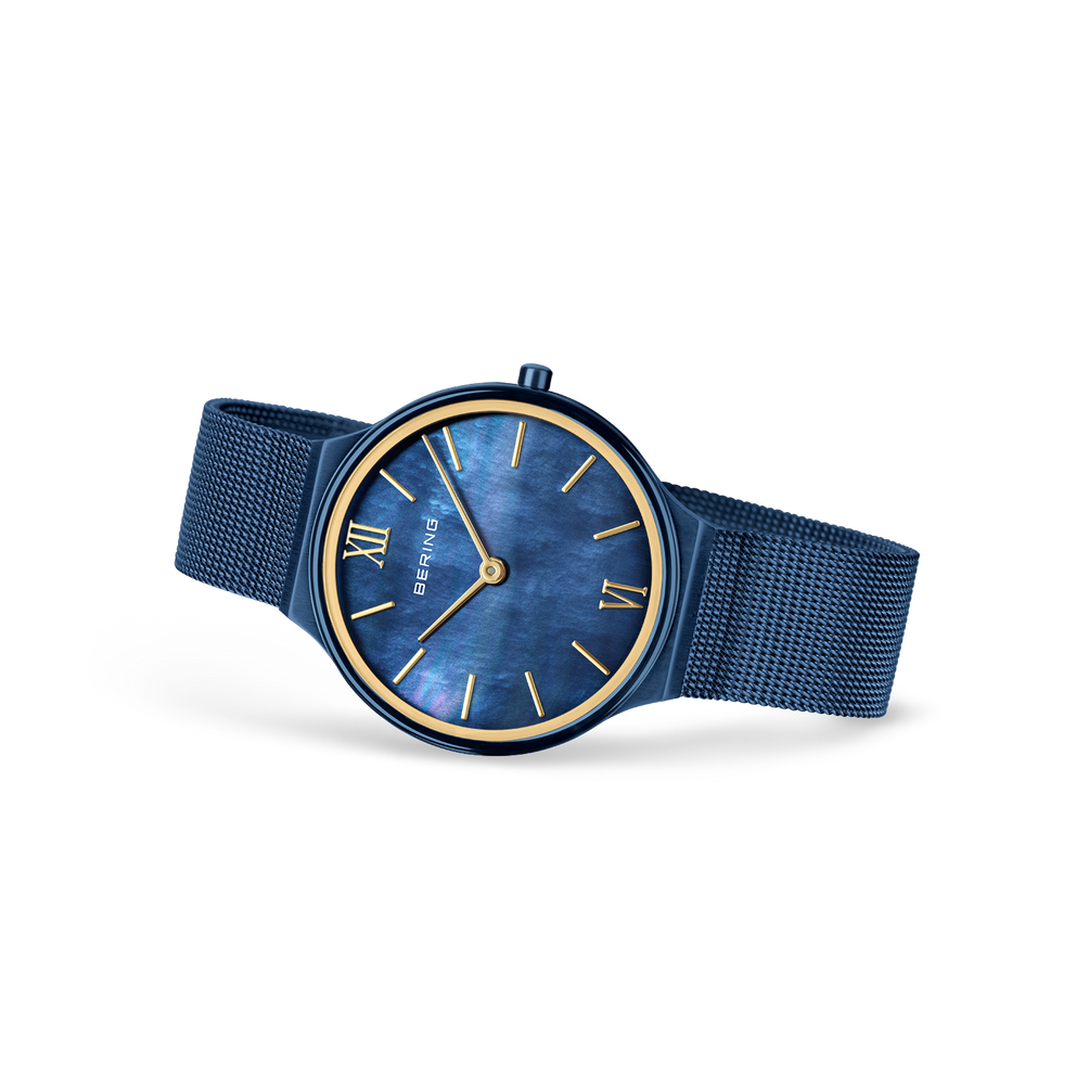 Blue dial watch with Roman numerals and gold hands, blue mesh strap, angled view