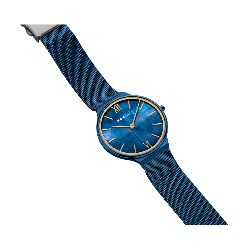 BERING watch with blue dial and gold indices, blue textile strap, angled view.