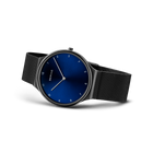 Reloj con esfera azul oscura, agujas minimalistas, cifras árabes y pulsera malla negra visto en ángulo