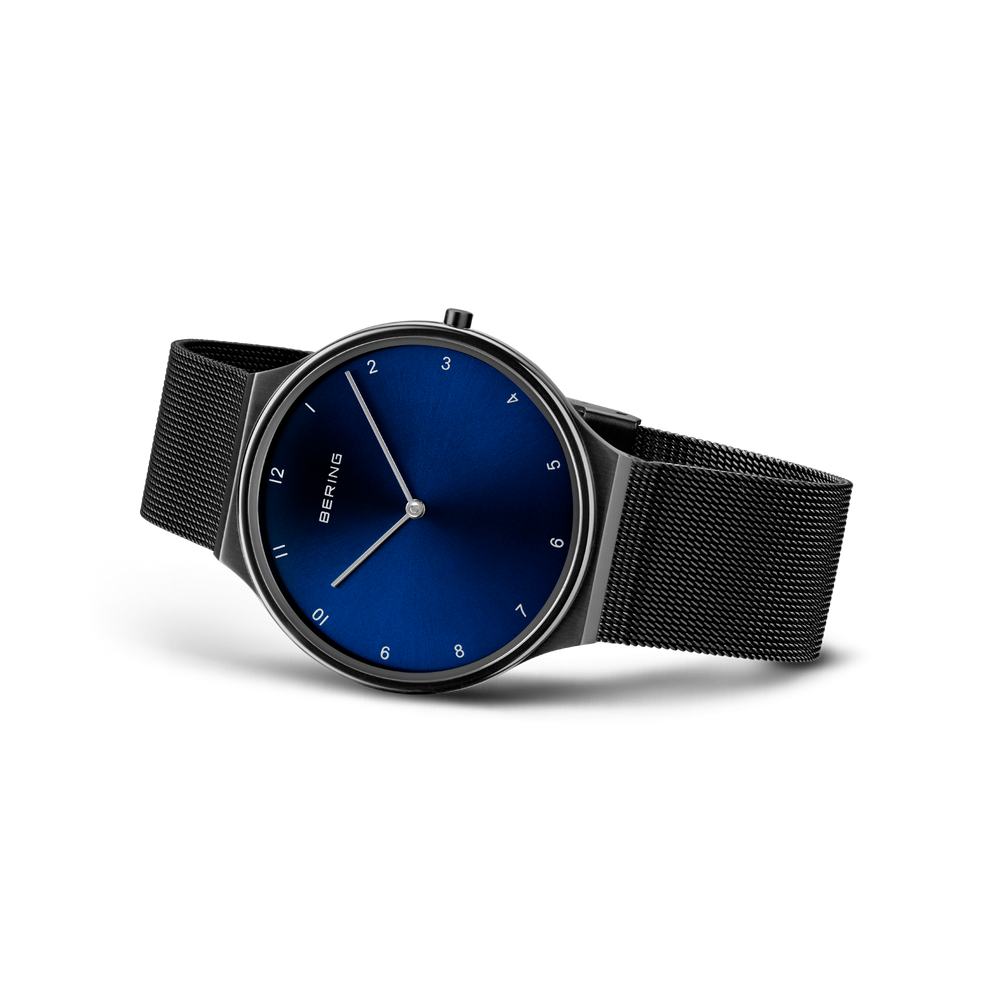 Reloj con esfera azul oscura, agujas minimalistas, cifras árabes y pulsera malla negra visto en ángulo