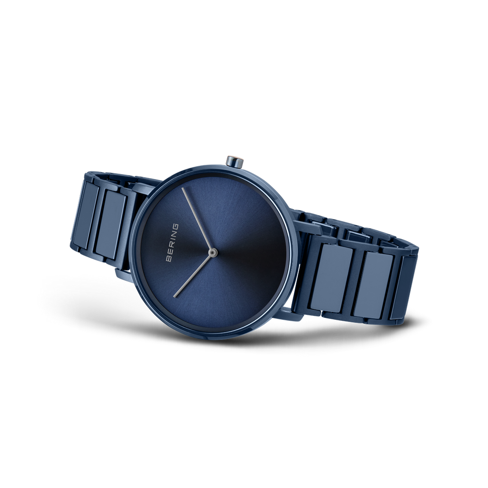 Dunkelblaues rundes Zifferblatt mit weißen Stundenindizes und dunkelblaues Metallarmband, seitlich fotografiert.