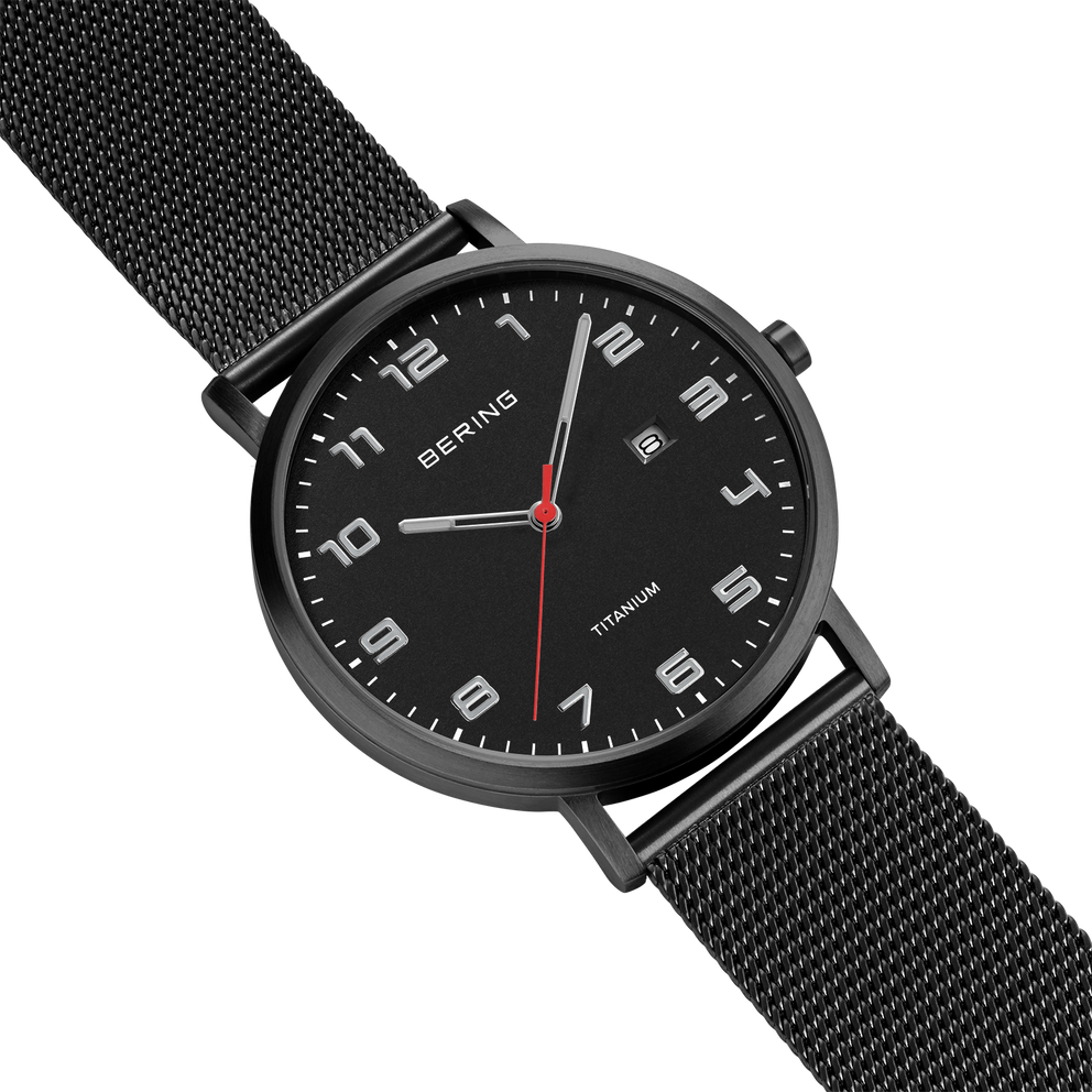 Quadrante nero con marcatori bianchi, cassa rotonda scura, cinturino mesh nero, vista angolata