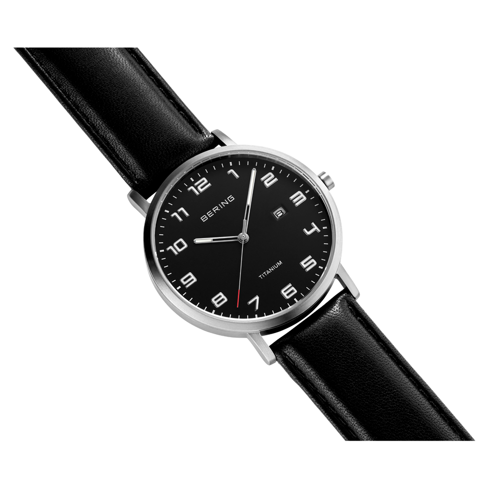 Round wristwatch with black leather strap, silver case, and black dial with Arabic numerals and date window, angled view.