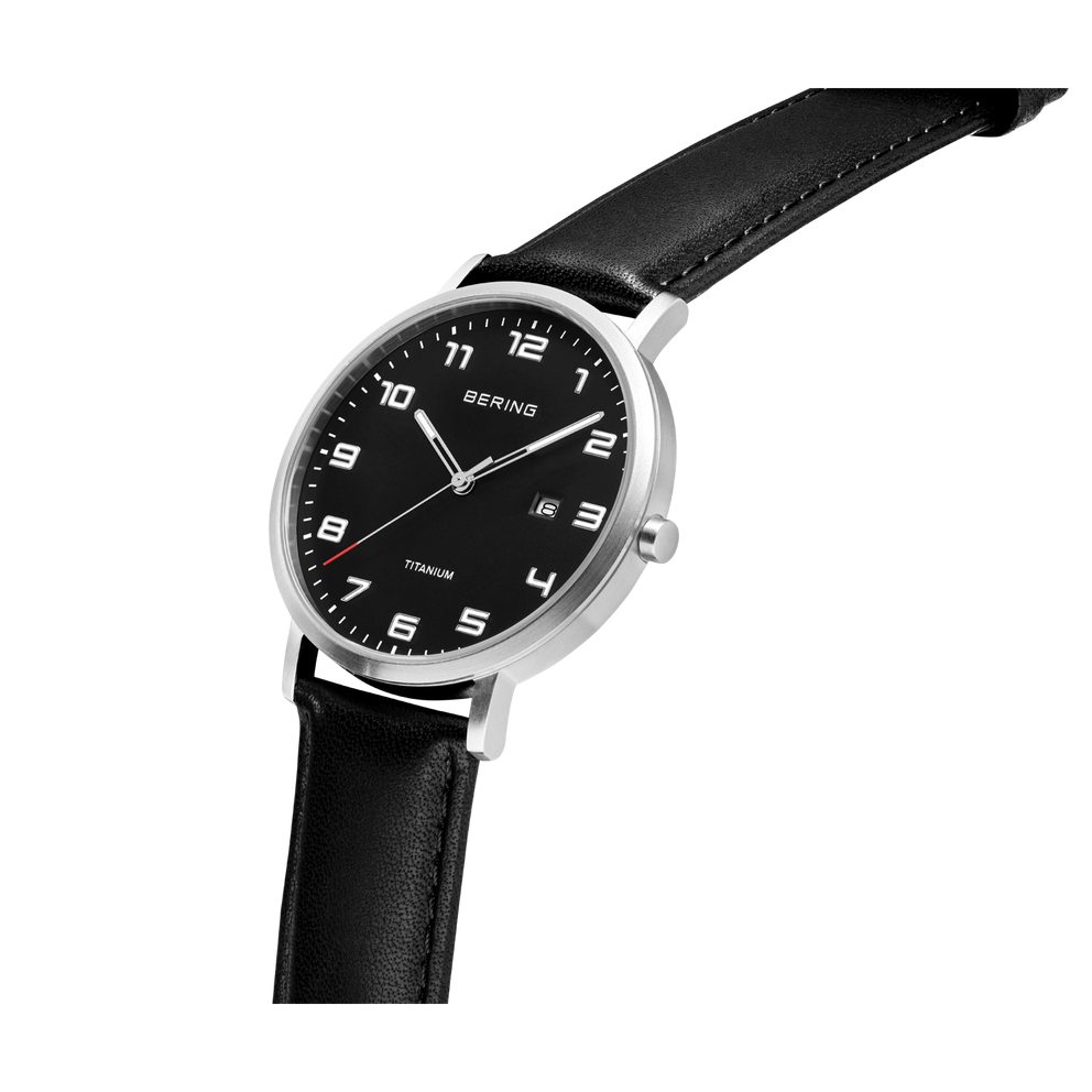 Round silver watch case with black dial, white hour markers and hands, black leather strap, shown at an angle.