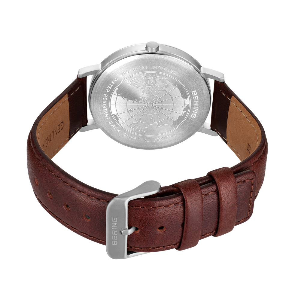 Watch shown from back with engraved silver caseback, brown leather strap, and metal buckle.