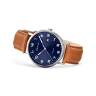 Wristwatch with navy dial, Arabic numerals, silver case, and tan leather strap, angled view