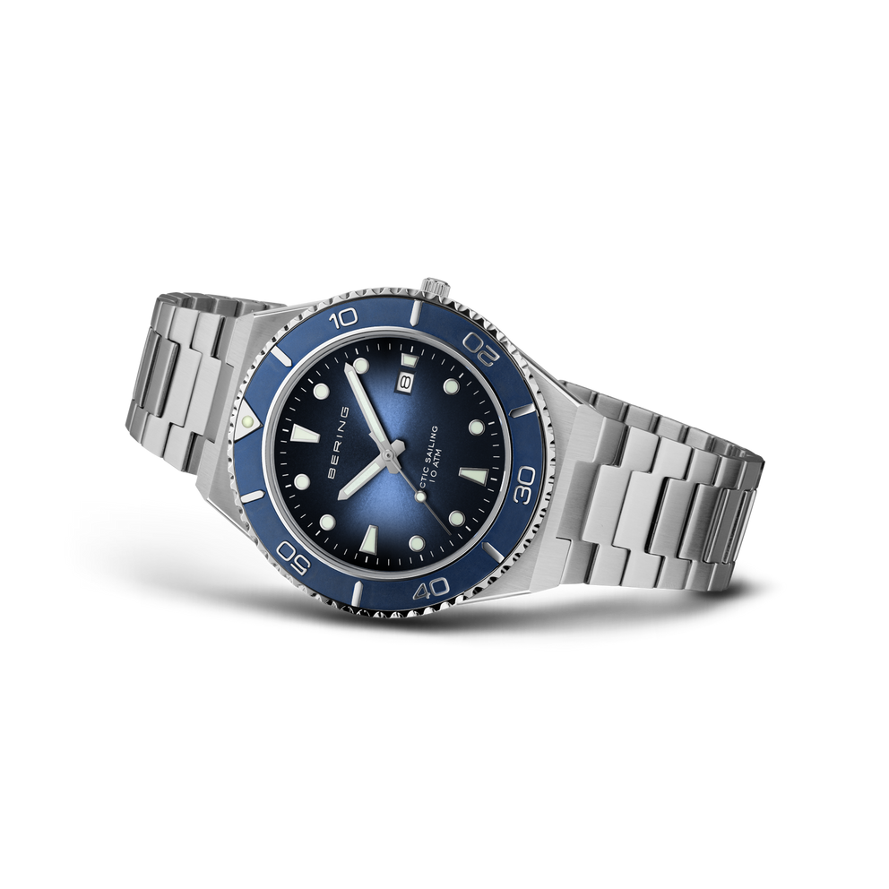 BERING wristwatch angled to show silver bracelet, dark blue dial with luminous indices, blue bezel, and blue hands.